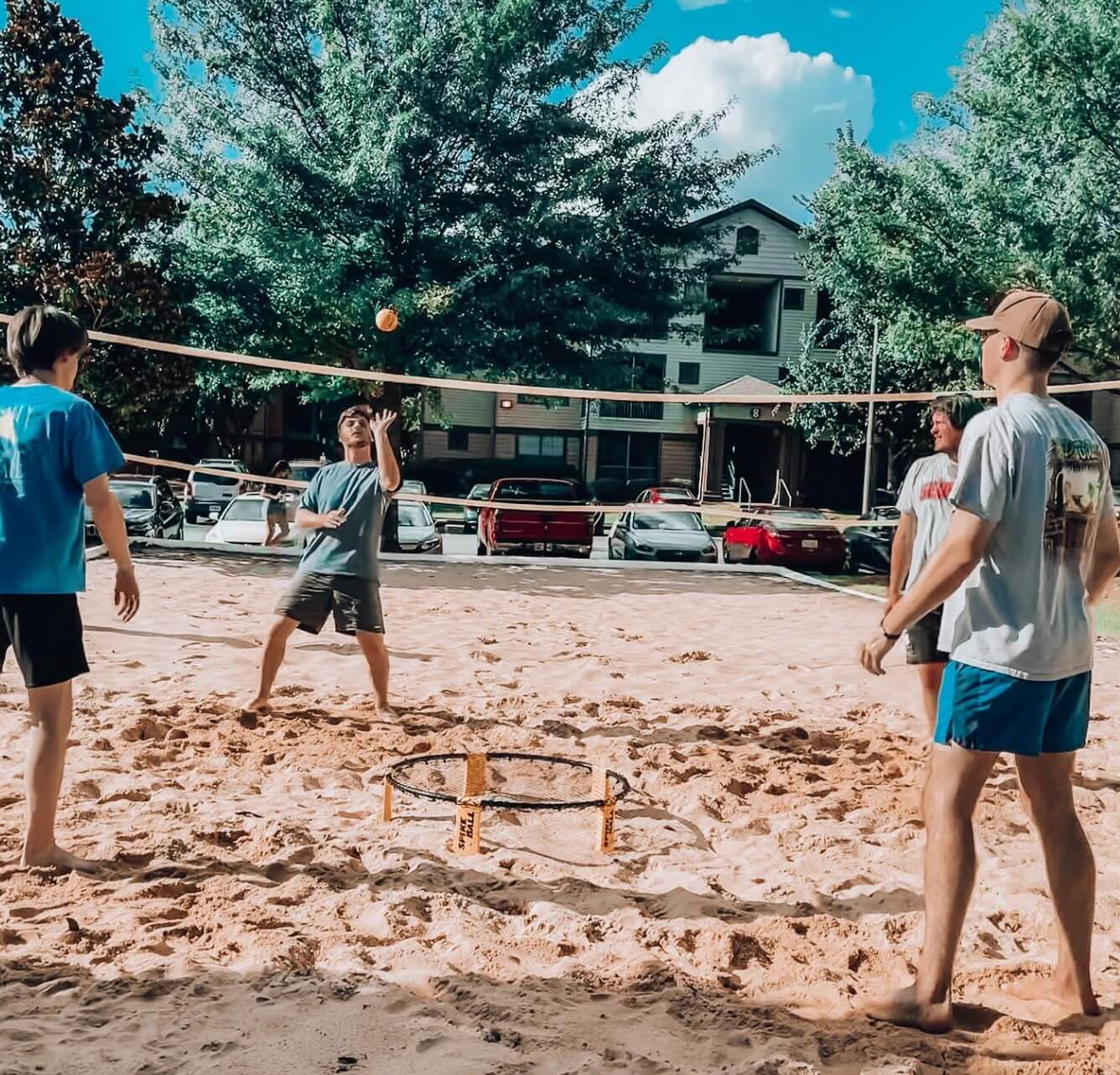 A group of friends enjoys a sunny day playing a ball game on a sandy court, savoring the casual, fun moments of outdoor activities.